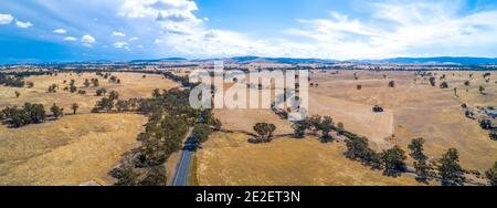 Kurvenreiche Straße und kleiner Bach, der an einem sonnigen Tag in Victoria, Australien, durch landwirtschaftliches Land führt - Luftpanorama Stockfoto