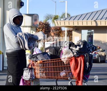 FRESNO, USA - Dec 30, 2020: Nahaufnahme einer schwarzen Obdachlosen Frau mit ihrem roten Korb voller Kleidung und Geldbörsen an einem sonnigen Tag draußen Stockfoto