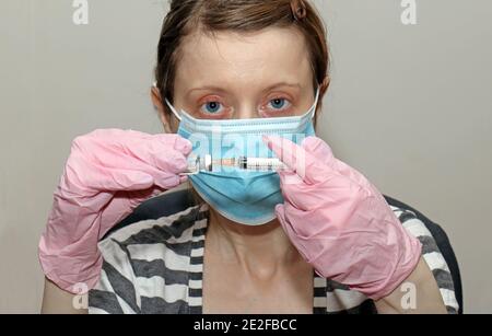 Junge Krankenschwester medizinische Arbeiter hält COVID-19-Impfstoff und Spritze während Tragen von medizinischen Handschuhen und Gesichtsmaske Stockfoto