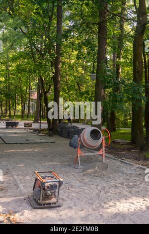 Bauarbeiten im Stadtpark. Betonmischer und Vibrationsplatte für die Reparatur von Pflasterplatten zum Sand. Selektiver Fokus. Stockfoto