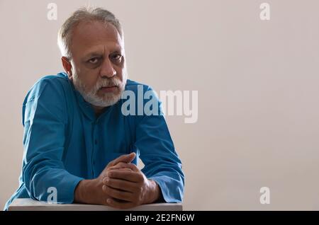 EIN ERWACHSENER MANN SITZT BESORGT UND SCHAUT AUF DIE KAMERA Stockfoto