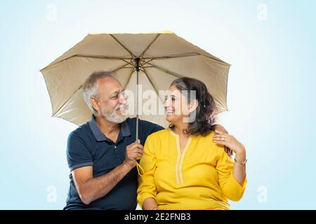 EIN ALTES PAAR SCHAUT SICH BEIM SITZEN GLÜCKLICH AN UNTER EINEM REGENSCHIRM Stockfoto