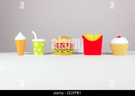Abwechslungsreiches Spielzeug Fast Food in Miniatur auf WEISSEM Hintergrund. Konzept der schädlichen künstlichen Nahrung Stockfoto