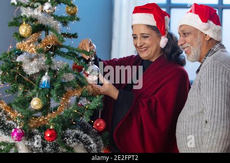 EIN GLÜCKLICHES ALTES PAAR, DAS ZUSAMMEN WEIHNACHTSBAUM SCHMÜCKT Stockfoto