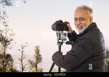 EIN ÄLTERER ERWACHSENER MANN SCHAUT GLÜCKLICH NACH HINTEN, WÄHREND ER AUF DIE BILDER KLICKT AUF SEINER KAMERA Stockfoto