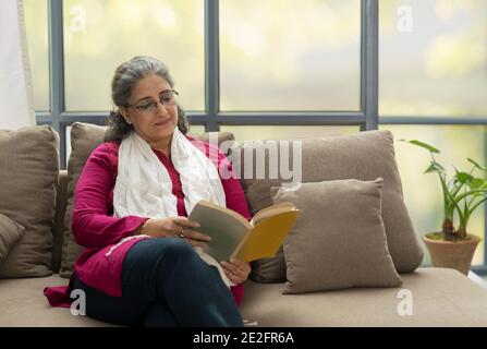 EINE ÄLTERE ERWACHSENE FRAU, DIE SITZT UND BUCH LIEST Stockfoto