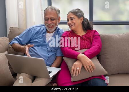 EIN GLÜCKLICHES PAAR, DAS ZEIT ZUSAMMEN VERBRINGT, WÄHREND ES EIN NOTEBOOK BENUTZT Stockfoto