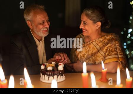 EIN GLÜCKLICHES ALTES PAAR, DAS SICH BEIM SCHNEIDEN ANSIEHT KUCHEN Stockfoto