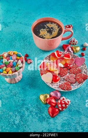 Valentinstag oder romantisches Abendessen mit Süßigkeiten Herzen, eine Tasse heißen Kaffee und elegante Tischeinstellung auf hellblauem Hintergrund Stockfoto