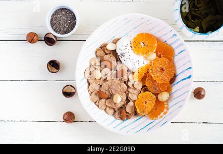 Schüssel mit Flocken mit Joghurt und Mandarine auf weißem Holztisch. Fitnessessen. Oben, Draufsicht, flach liegend Stockfoto