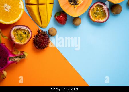 Zusammensetzung der tropischen Sommerfrüchte. Horizontaler Schuss aus Papaya, Rambutan, Mango, Passionsfrucht, Longae, Erdbeere isoliert auf pastellblauem orangefarbenem Backg Stockfoto
