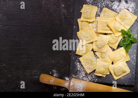 Frische Ravioli mit Basilikum auf dunklem Brett, Draufsicht Stockfoto