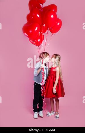 Valentinstag. Kleiner Junge küssen schöne kleine Mädchen auf rosa Hintergrund. Kinder mit Herzballons Stockfoto