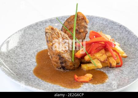 Ochsenschwanz-Timbale geschmort, mit rotem Pfeffer und pommes auf einem Teller mit weißem Hintergrund Stockfoto