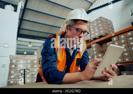 Männlicher Fabrikingenieur, der eine Brille mit einem digitalen Tablet trägt, auf das er sich stützt Tabelle Stockfoto