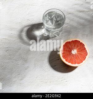 Sommer Schreibwaren Stillleben Szene. Nahaufnahme von geschnittenen Grapefruitfrüchten auf weißem Tischhintergrund im Sonnenlicht. Leere Papierkarten, Einladungen Mockup Szene Stockfoto