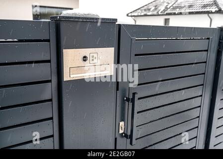 Ein modernes Videotelefon mit Briefkasten und kabellosem Kartenleser, in anthrazitfarbenem Panelzaun montiert, sichtbares Wicket, es regnet im Winter, in Th Stockfoto