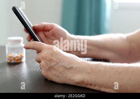 Ältere Frau mit Smartphone am Tisch sitzend, Handy in faltigen weiblichen Händen. Konzept der Online-Kommunikation im Ruhestand Stockfoto