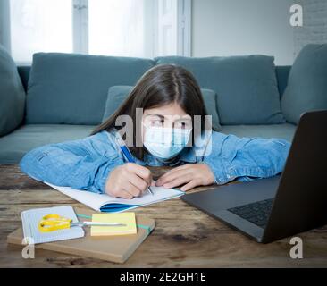 Gelangweilt und deprimiert Teenager-Mädchen mit Gesichtsmaske auf Laptop Studieren zu Hause in Online-Bildung Klasse als High School Wegen des neuen COVID-19 geschlossen bleiben Stockfoto