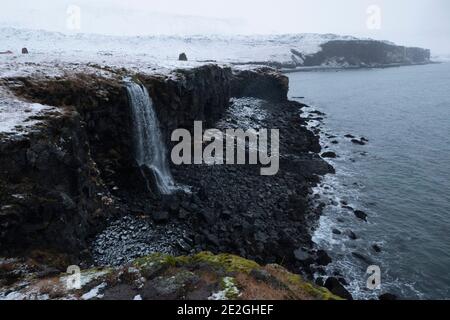 Majestätischer schneebedeckter Wasserfall über der Meeresklippe, Arnastapi, Island Stockfoto