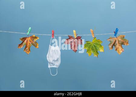 Gesichtsmaske hängt auf Wäscheleine mit Herbstblättern Stockfoto