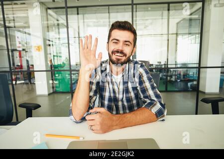 Freundliche Brünette Kerl winkt seine Hand während eines Video-Call Stockfoto