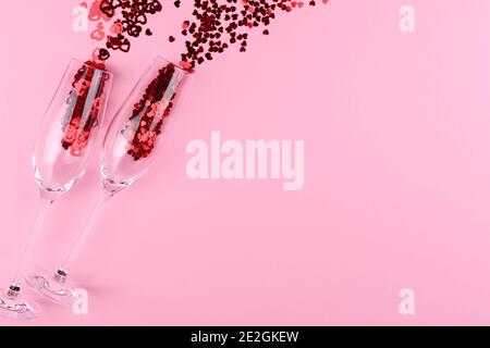 Zwei Gläser Champagner gefüllt mit herzförmigen Pailletten auf einem rosa Hintergrund valentinstag. Stockfoto