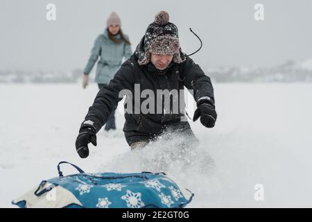 Mann, der mit Freundin in die Schneeröhre fällt. Junge glückliches Paar zu Fuß im Wintertag Stockfoto