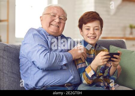 Glücklicher Opa und kleiner Enkel sitzen auf dem Sofa und spielen Spiele auf dem Handy Stockfoto