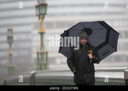 Ein Mann, der einen Regenschirm hält, während er über die Westminster Bridge in London geht. Stockfoto