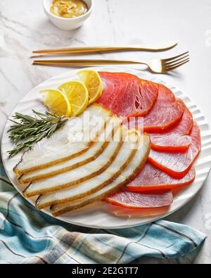 Geräucherter Fischteller: Kalter geräucherter Heilbutt und kalte geräucherte Thunfischscheiben auf einem weißen Teller mit Rosmarinzweigen, Zitronenkeilchen und englischem Senf Stockfoto