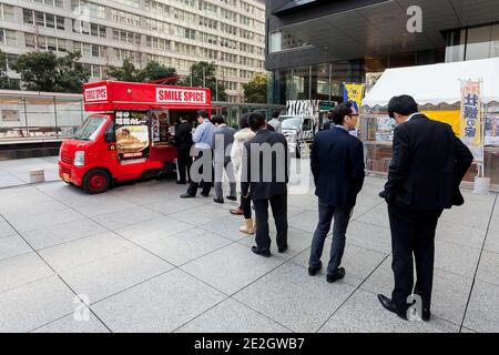 Japanische Salarymen stehen für ein Mittagessen in einem Kleinbus auf dem Sankai Plaza in Otemachi, Tokio, Japan, an. Stockfoto