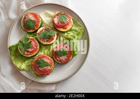 Mini Pizza Snack aus dem Ofen gebacken Zucchini Scheiben, Tomaten, Parmesan-Käse und Petersilie garnieren auf einem Teller mit Salatblättern, weiß bemalten Tisch mit Stockfoto