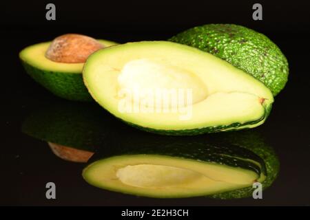 Ein Ganzes, eine Hälfte und eine Hälfte mit einem Knochen, grün appetitlich frisch diätetisch reifen leckeren Avocados, auf schwarzem Hintergrund. Im Vordergrund, im Fokus - Stockfoto