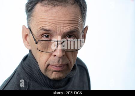 Ein älterer Mann mit einem faltigen Gesicht blickt über seiner Brille auf die Kamera. Porträt eines Rentners aus Russland auf weißem Hintergrund im Studio. Stockfoto
