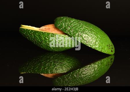 Zwei Hälften grüner diätetischer appetitlich frischer natürlicher reifer leckerer Avocados, auf schwarzem Hintergrund, einer übereinander liegend. Stockfoto