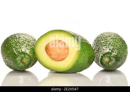 Zwei ganze und eine Hälfte mit einem Knochen, zwischen ganzen Früchten, reifen Bio-grünen Avocados, auf weißem Hintergrund. Stockfoto