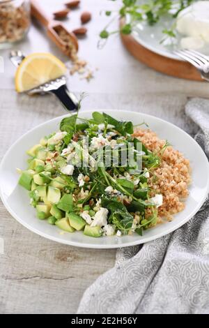 Glutenfreier grüner vegetarischer Salat aus mikrogrünen Sprossen Erbsen, Avocado, Quinoa, Spinat, gewürzten zerdrückten Mandeln mit Scheiben Feta-Käse Stockfoto