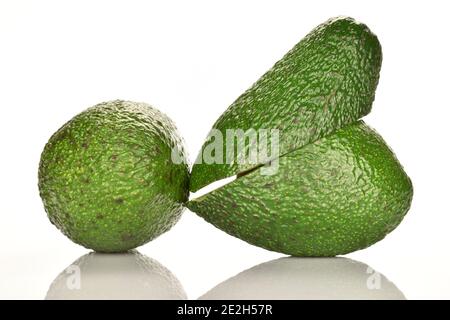 Eine ganze und zwei Hälften, quer geschnitten, reife grüne Avocados, auf weißem Grund. Stockfoto