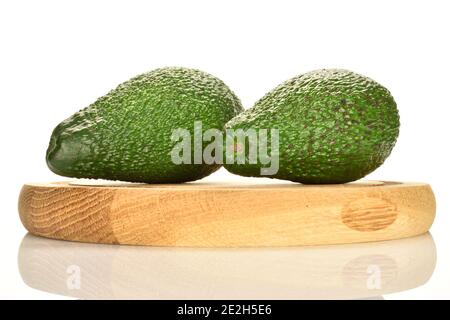 Zwei ganze grüne, reife Avocados, die auf einem runden Ständer aus Holz auf weißem Grund liegen. Stockfoto