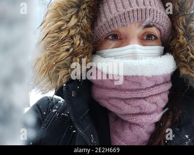 Nahaufnahme Porträt der jungen kaukasischen Frau in rosa Hut mit Pelz Pompon, Wollschal und schwarzem Mantel. Frau genießt den Schneesturm genießen Winter Stockfoto