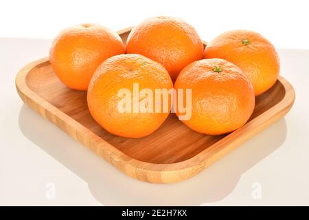 Ein paar ganze leuchtend orange reife saftige Mandarinen, liegen auf einem Bambusblech, auf weißem Hintergrund. Die nächste Mandarin, im Vordergrund im Fokus. Stockfoto