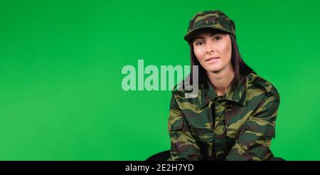 Banner – Langformat. Porträt einer niedlichen Frau in Militäruniform Blick in die Kamera auf einem grünen Hintergrund mit leeren Seitenraum. Stockfoto