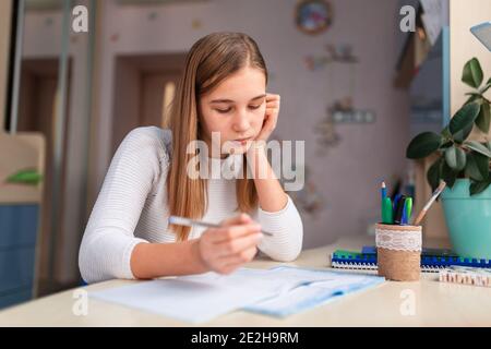 Schöne müde Schulmädchen studieren zu Hause tun Schule Hausaufgaben. Schulungsbücher und Notizbuch auf dem Tisch. Fernunterricht Online-Bildung Stockfoto