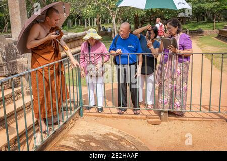 Chinesische Touristen hören zu, wie ein buddhistischer Mönch die Bedeutung erklärt Der 'Moonstone' auf einer Führung durch die Antike Standort von Polonnaruwa in Sri LAN Stockfoto