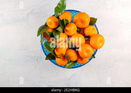 Orangefarbene Mandarinen mit grünen Blättern in blauer Platte auf weißem Steingrund. Blick von oben. Speicherplatz kopieren. Draufsicht Stockfoto