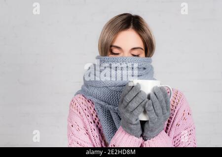 Junge Frau in warmen Schal gehalten Tasse auf weiß gewickelt Hintergrund Stockfoto