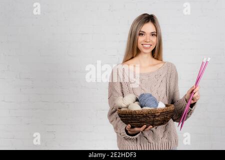 Positive Frau in Strickpullover mit Stricknadeln und Wolle Garn auf weißem Hintergrund Stockfoto