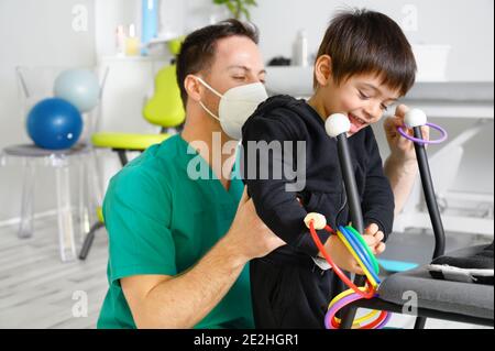 Kind mit zerebraler Lähmung auf Physiotherapie in einem Kindertherapiezentrum. Junge mit Behinderung macht Übungen mit Physiotherapeuten in Reha-Zentrum. Hochwertige Fotos. Stockfoto