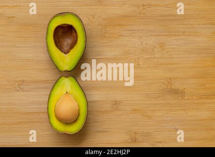 Zweischneidende halbe Avocados mit einzigartiger Anordnung auf Bambus-Schneidebrett, Draufsicht Bild, Platz für Kopie und Design. Stockfoto